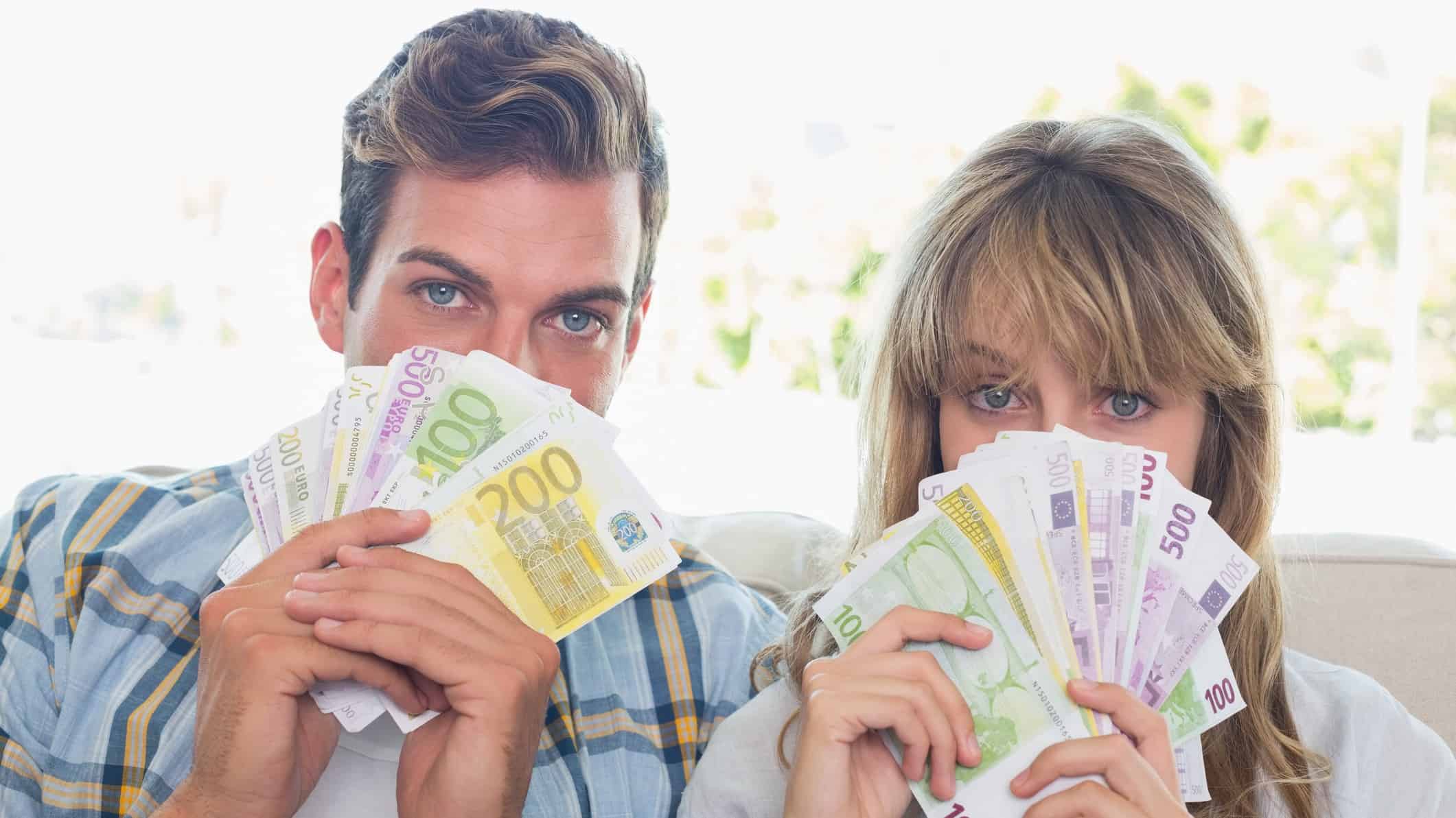 Man and woman holding up money over the bottom half of their face, symbolising dividends.