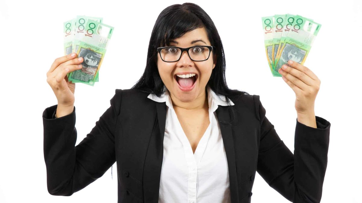 excited young female in business attire and wearing glasses is holding up $100 notes in both hands.