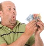 An excited male investor looks at some Australian bank notes held in his hand with an astounded look on his face
