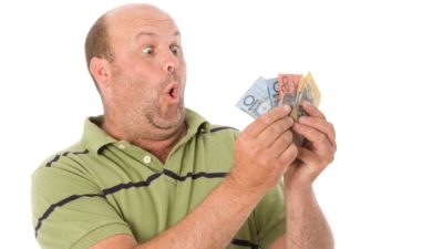 An excited male investor looks at some Australian bank notes held in his hand with an astounded look on his face