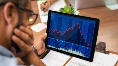 Man with his hand on his face looking at a falling share price chart on a tablet.