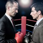 Two men in suits face off against each other in a boxing ring.