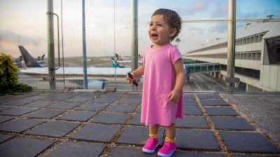 A young girl cries at an airport with planes lining up in the background.