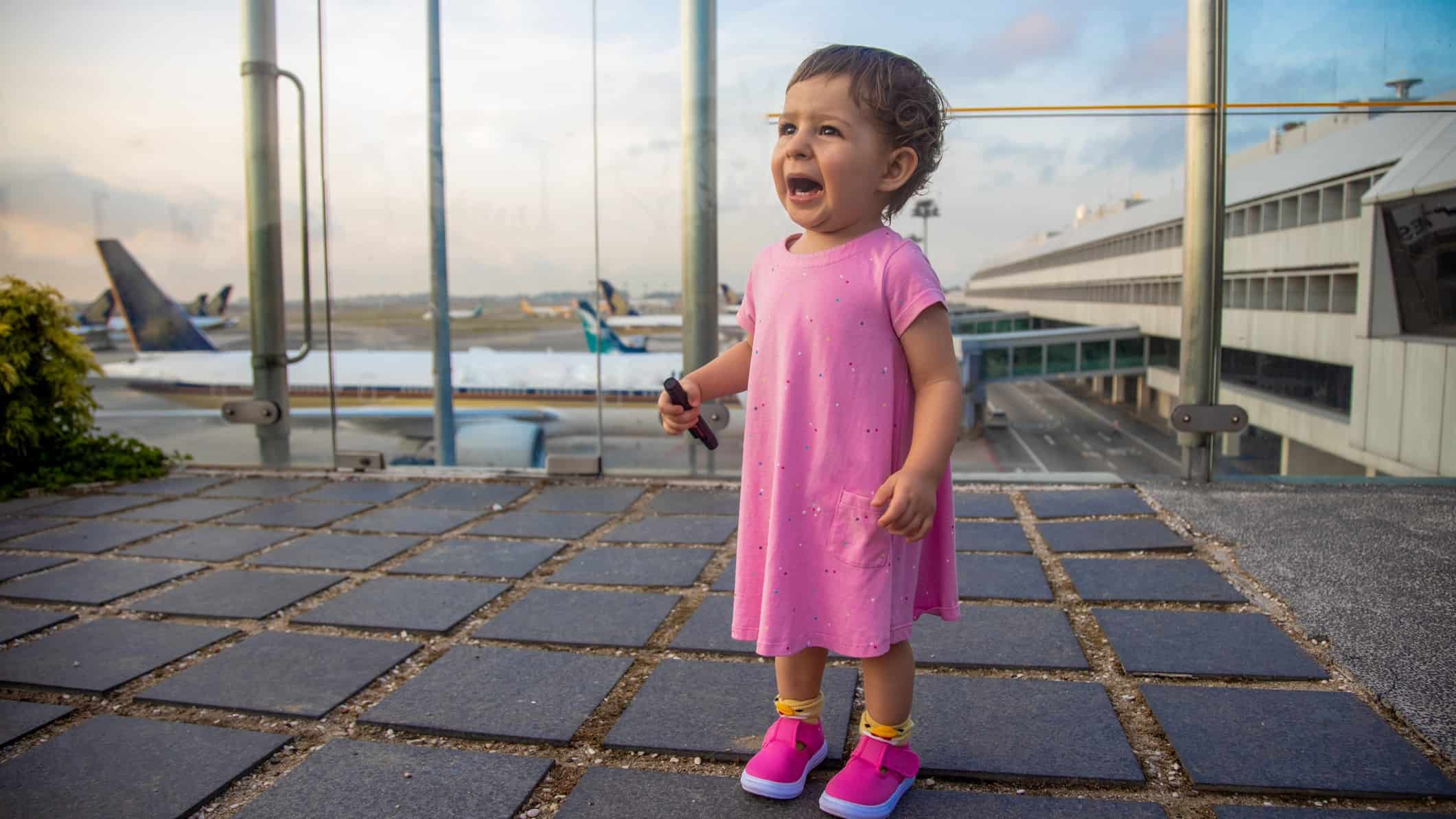 a young girl cries at an airport with planes lining up in the backbround.