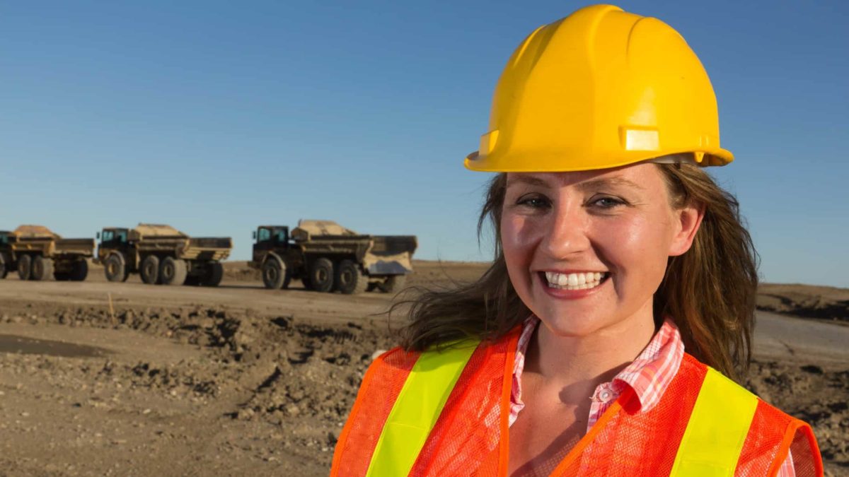 Female South32 miner smiling with mining machinery in the background.