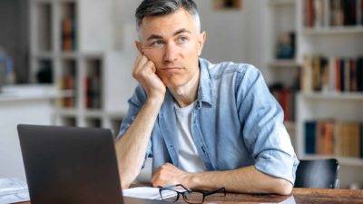 Bored man sitting at his desk with his laptop.