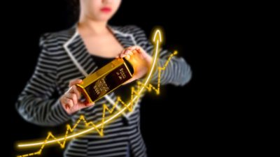 a woman in a business suit holds a large solid gold bar in both hands with a superimposed image of a gagged gold line tracking upwards and featuring a swooping curved arrow pointing upwards.