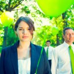 A group of businesspeople hold green balloons outdoors.