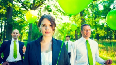 A group of businesspeople hold green balloons outdoors.