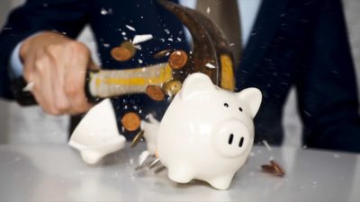 A man smashes open a piggy bank with a hammer representing an ASIC fine received by Westpac