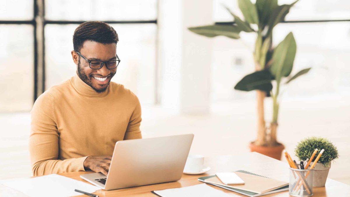 A young man sits at his desk working on his laptop with a big smile on his face due to his ASX shares going up and in particular the Computershare share price