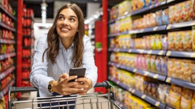 Happy woman looking for groceries. as she watches the Coles share price and Woolworths share price on her phone