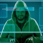 a man in a hoodie grins slyly as he sits with his hands poised on a keyboard. He is superimposed with a graphic image of a computer screen asking for a password, suggesting he is a hacker.