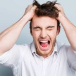 A young male investor wearing a white business shirt screams in frustration with his hands grasping his hair after ASX 200 shares fell rapidly today and appear to be heading into a stock market crash