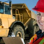 Female miner smiling in front of a mining vehicle.