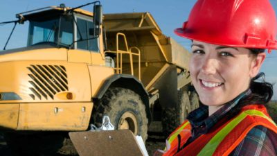 Female miner smiling in front of a mining vehicle.