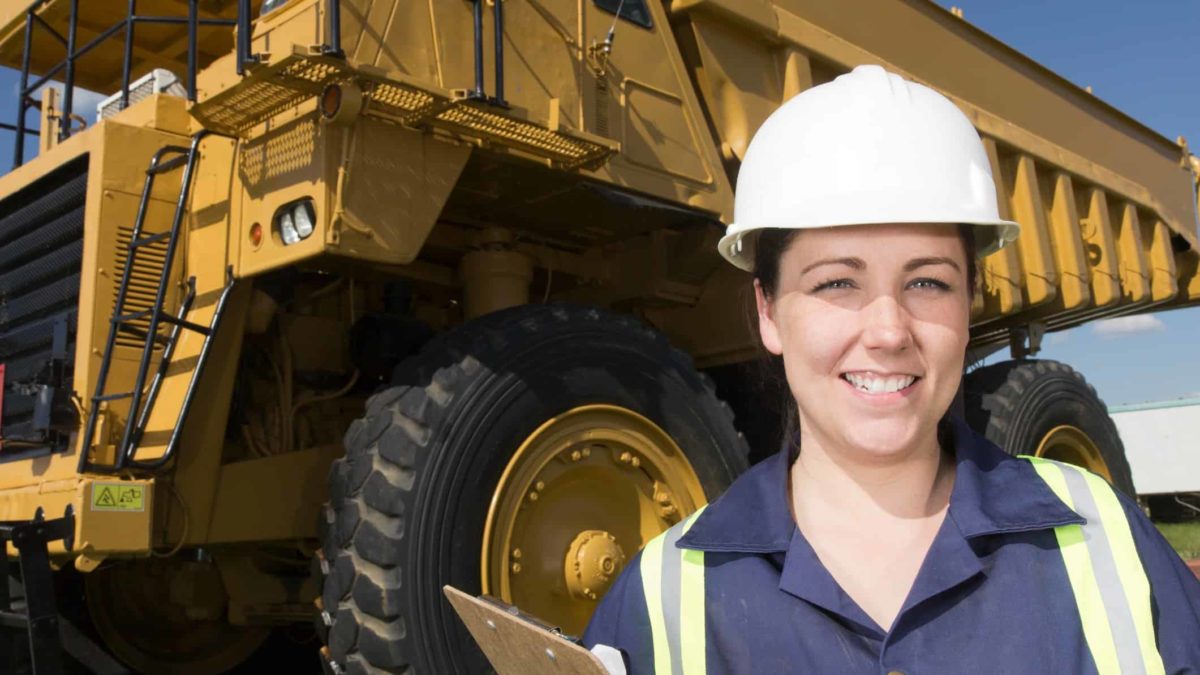 Female miner smiling in front of a mining vehicle as the Pilbara Minerals share price rises