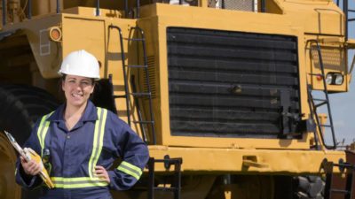 Female miner smiling in front of mining vehicle.