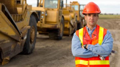 Man standing in a mine with mining vehicles.