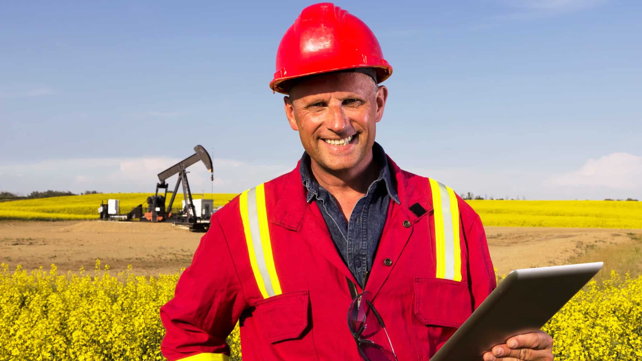 Happy man standing in front of an oil rig.