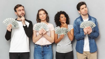 Four investors stand in a line holding cash fanned in their hands with thoughtful looks on their faces.