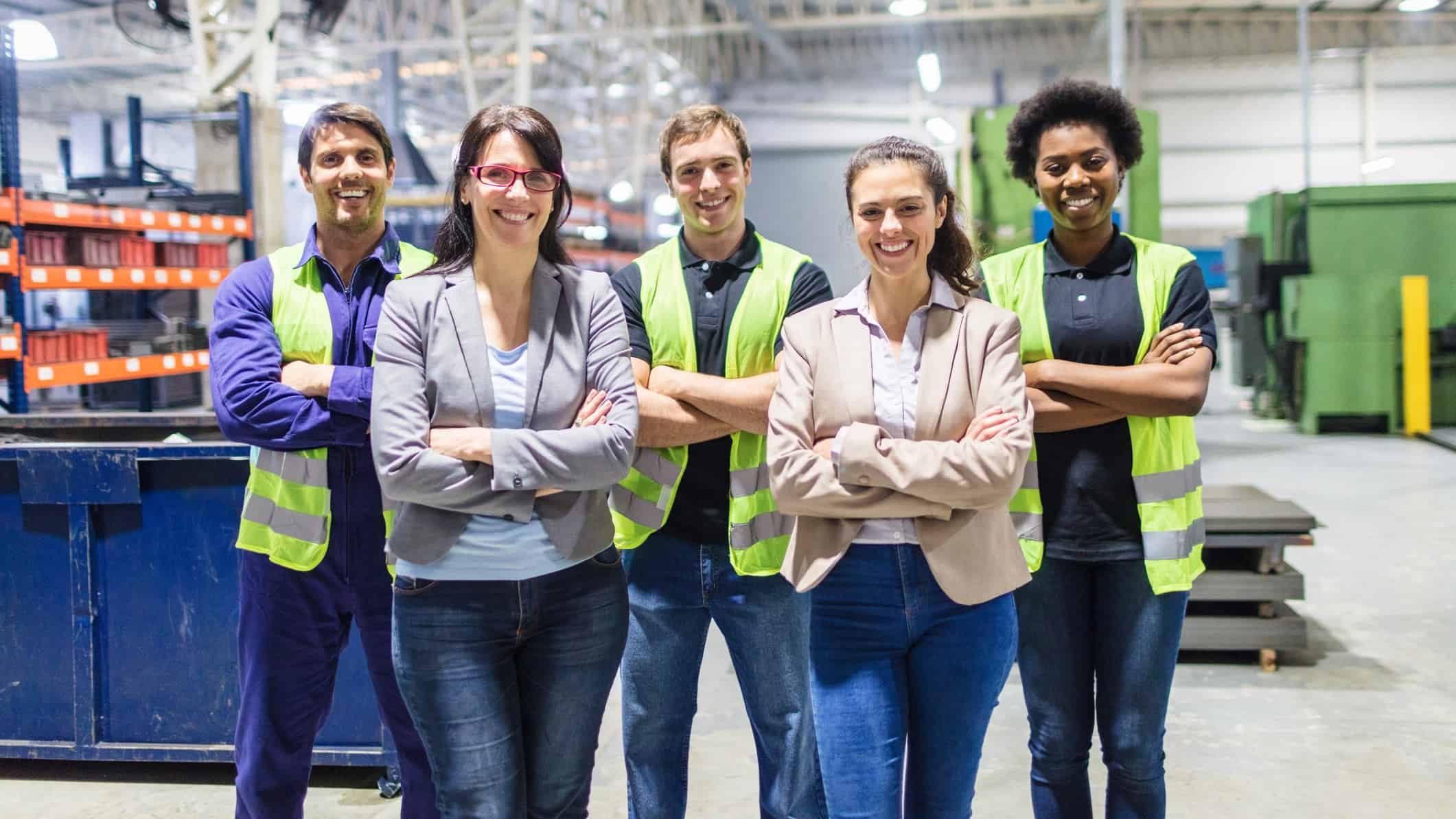Five factory workers and professionals standing and smiling.