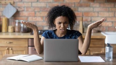 A woman puts up her hands and looks confused while sitting at her computer.