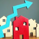 Increasing blue arrow with wooden property houses representing a rising share price.