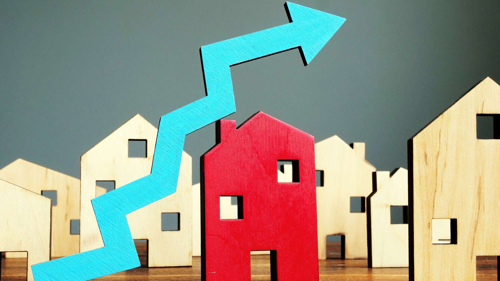 Increasing blue arrow with wooden property houses representing a rising share price.