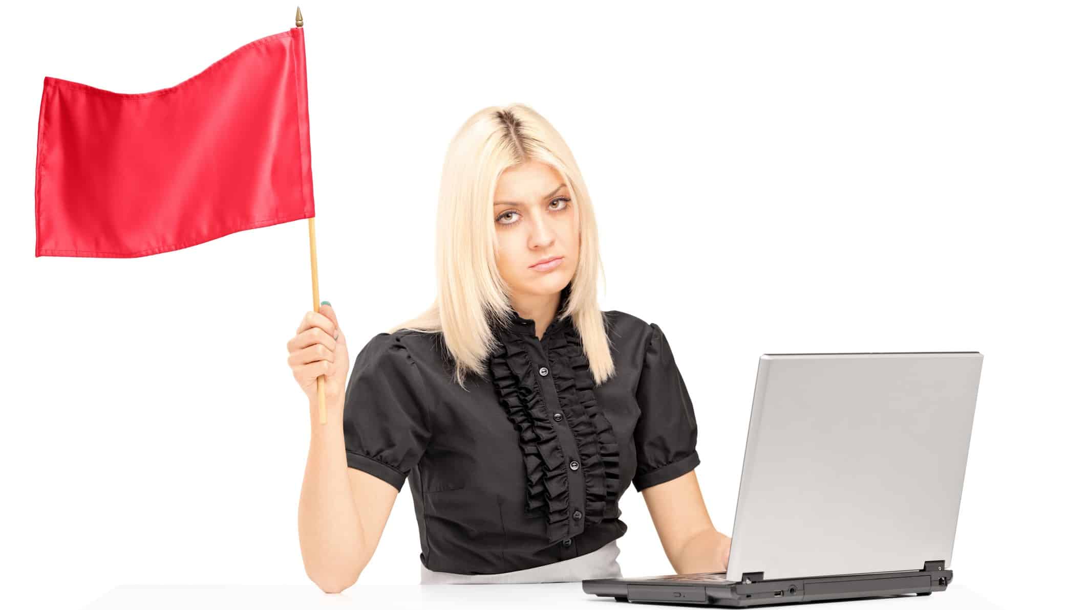 A business woman looks unhappy while she flies a red flag at her laptop.