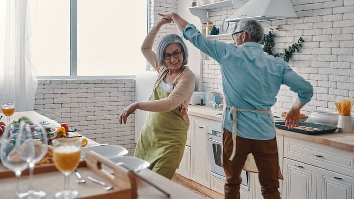 a mature aged couple dance together in their kitchen while they are preparing food in a joyful scene as the Breville share price rises on the back of a 25% profit surge