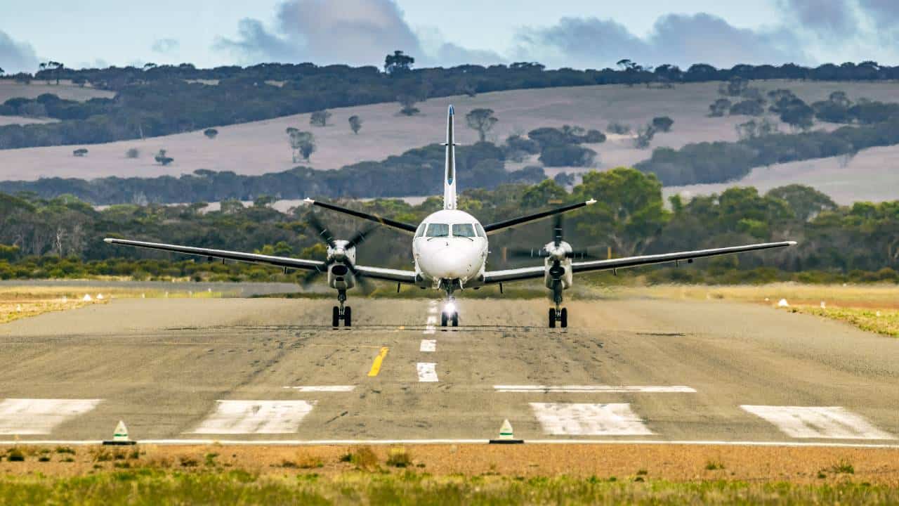 A small propeller plane taxies down a regional airport's runaway with beautiful mountains in the background representing the Regional Express Holdings business which is a competitor of Qantas