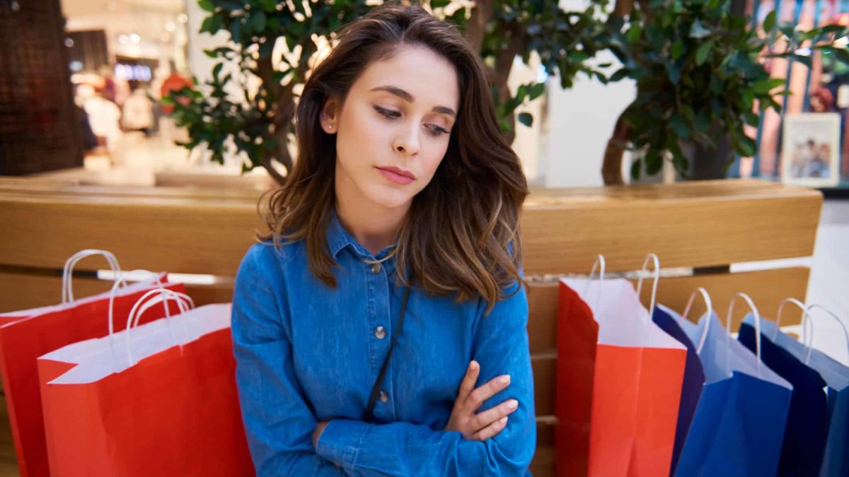 Sad shopper sitting down with five shopping bags next to her