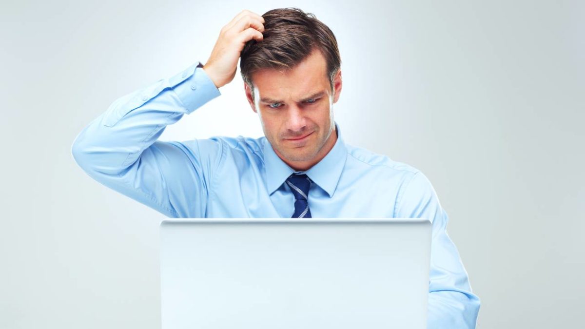 An ASX investor in a business shirt and tie looks at his computer screen and scratches his head with one hand wondering if he should buy ASX shares yet