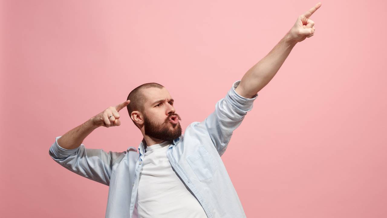 A bearded man holds both arms up diagonally and points with his index fingers to the sky with a thrilled look on his face over these rising Mineral Resources share price