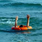 A person holds their hands up through the middle of a rubber lifesaving ring while swimming in relatively calm conditions at a beach.