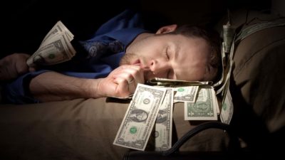 A man sleeping in bed with money around him.
