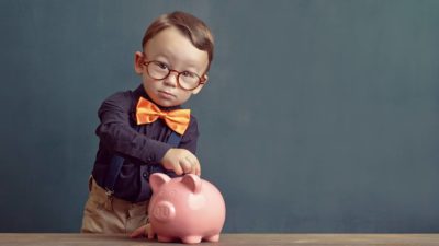 Kid putting a coin in a piggy bank.