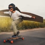 Kid on a skateboard with cardboard wings soars along the road.