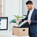A man packs up a box of belongings at his desk as he prepares to leave the office.