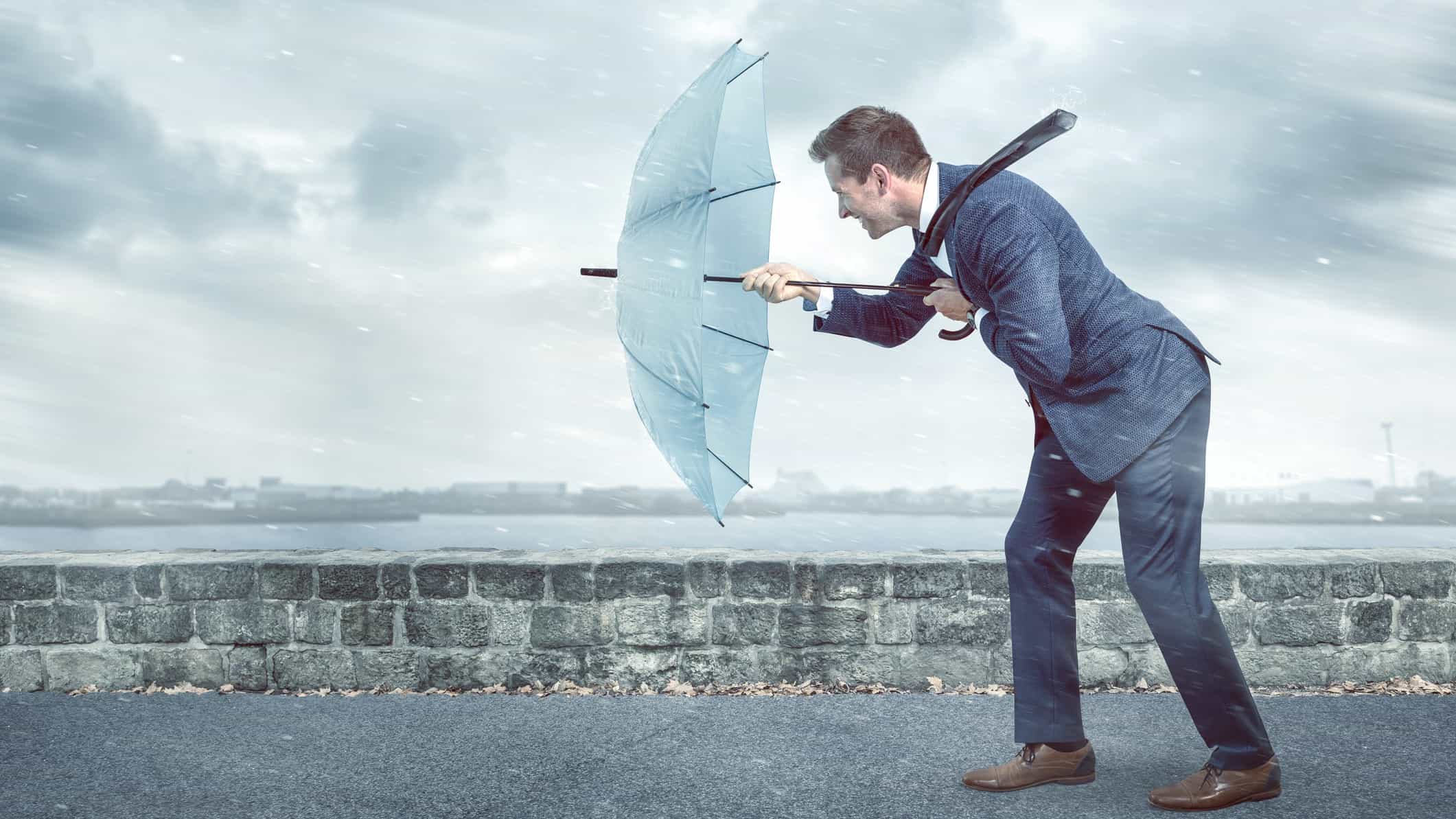 Businessman weathers headwinds with an umbrella.
