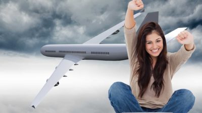 a smiling young woman sits and raises her hands in celebration in the foreground of a jet plane flying out of dark, stormy skies.