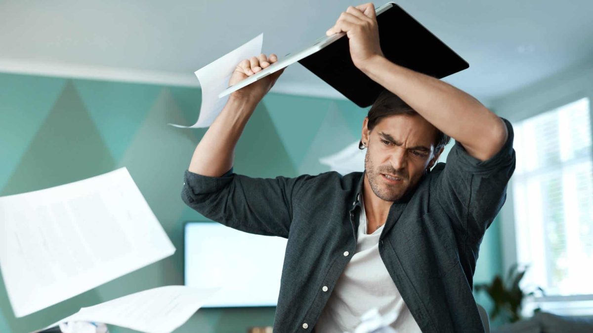 A male investor erupts into a tantrum and holds his laptop above his head as though he is ready to smash it, as paper flies around him, as he expresses annoyance over so many new 52-week lows in the ASX 200 today