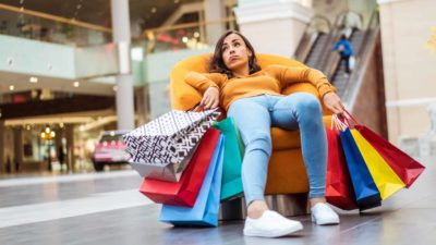 Sad shopper sitting on a sofa with shopping bags.