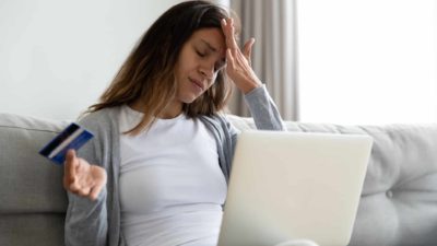 Upset woman with her hand on her forehead, holding a credit card.