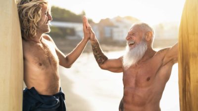 Two surfers, one older and one younger, high five with big smiles on their faces.