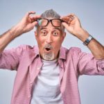 A man raises his reading glasses in a look of surprise.