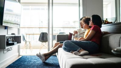 A family sits on their couch, eyes glued to the television.