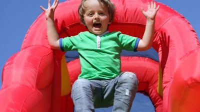 A boy bounces off a big red inflatable slide with a smile on his face.