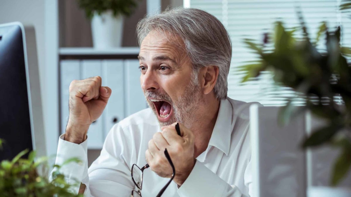 A man clenches his fists with glee having seen the share price go up on the computer screen in front of him.